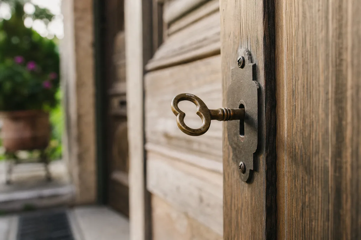 Old brass key in the lock of a weathered wooden front door