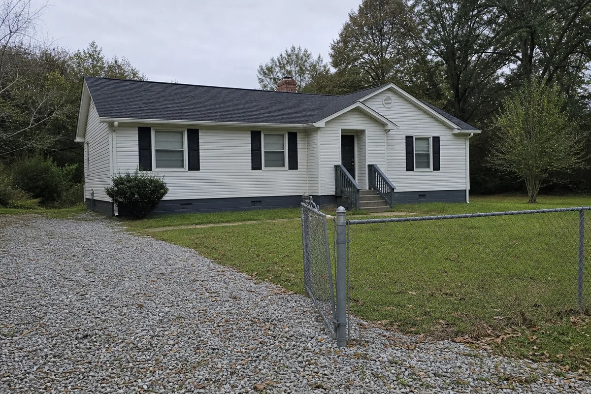 Small single-story rental house in Georgia with a chain-link fence and gravel driveway