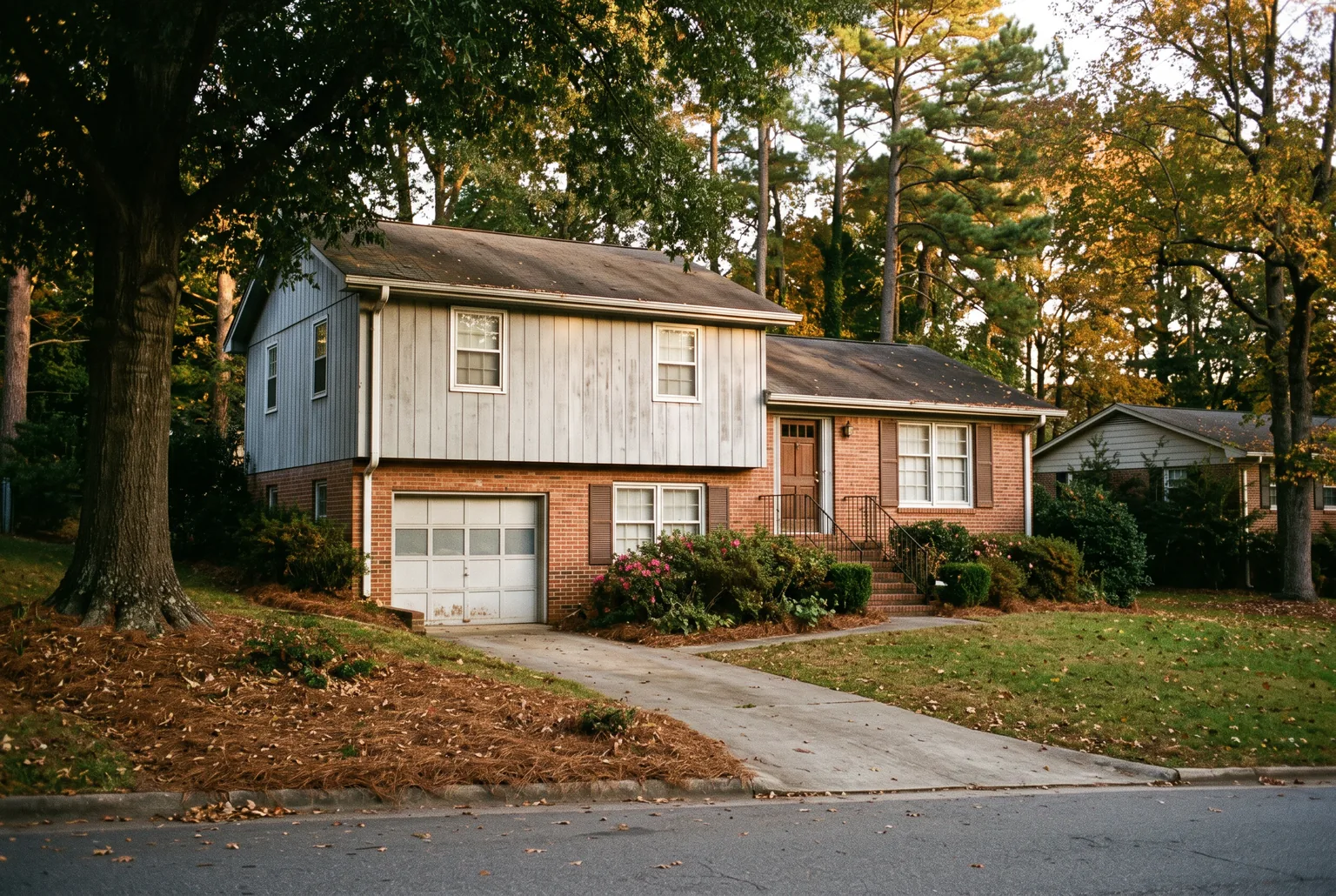 1970s split-level house with red brick and faded gray siding under tall pines