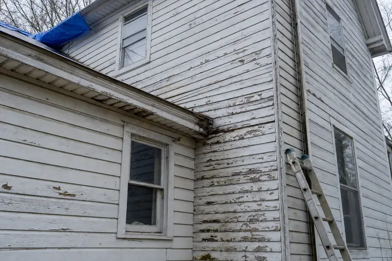 Corner of an older wood-sided house with peeling paint and a tarp over the roof